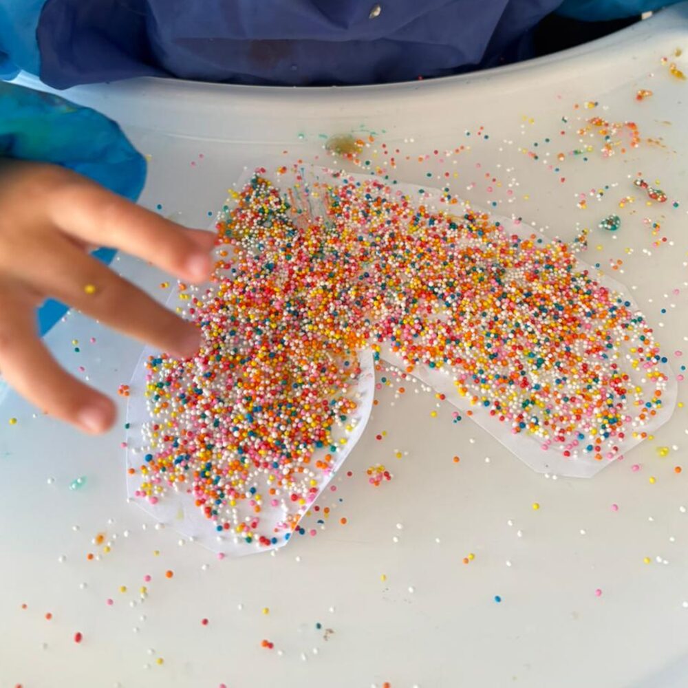 Hands exploring sprinkles on a tray